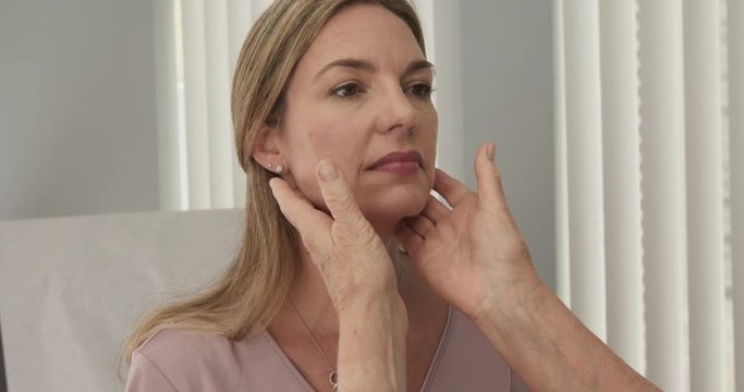 Close up of senior doctor feeling lymph nodes on female Caucasian patient in exam room. Middle aged woman visiting primary care physician at clinic or hospital. Slow motion 4k