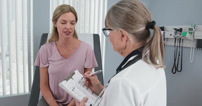 Over the shoulder shot of woman talking to her primary care doctor in exam room. Middle aged patient having appointment with female senior physician. Slow motion 4k