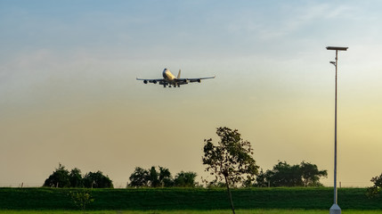 Commercial airline. Passenger plane landing above green trees at airport with beautiful sunset  sky and clouds. Arrival flight. Wire fence and green hedge fence and solar cell panels at the airport.