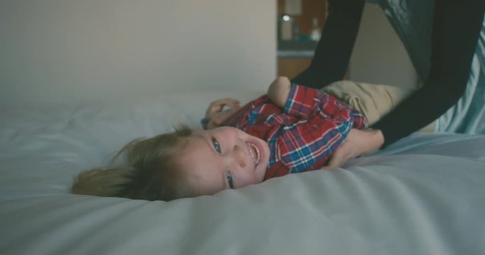 Young mother tickling her toddler on a bed in hotel room