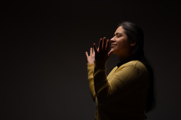 Hispanic Christian Woman Praying or Talking to God on Dark Grey Background