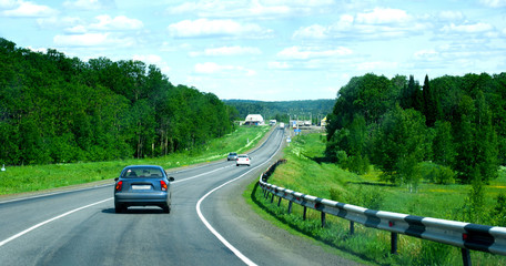 cars on asphalt road through wild forest near village