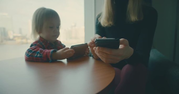 Mother and toddler using smartphones by window in city