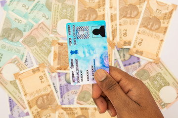person holding PAN card on stack of Indian new currency notes.
