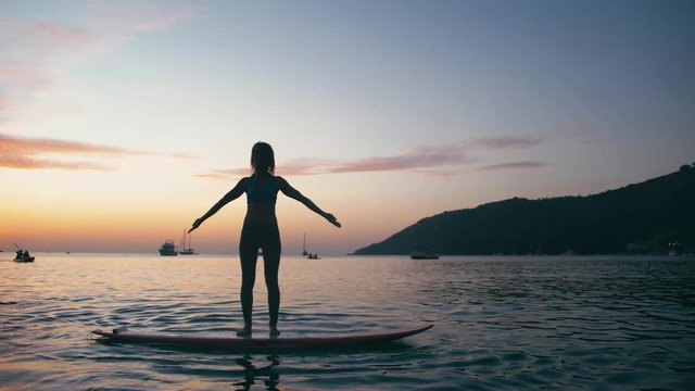 Young woman doing yoga on sup board with paddle at sunset. Concept of harmony with the nature, free and healthy living, freelance, remote business.
