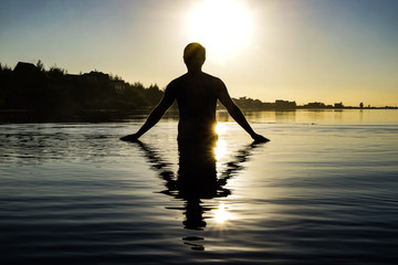 outline photo of a man coming out of the water on the background of a beautiful setting sun