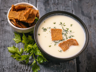 Cream cauliflower soup with herbs and crackers on a black table.