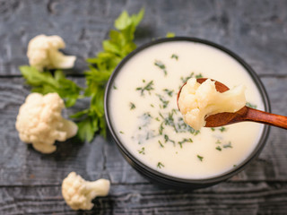 Spoon with a piece of cauliflower over a bowl of cream soup.