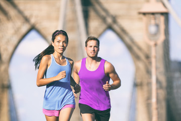 New York city runners running training for marathon on Brooklyn bridge NYC in urban cityscape. Fit...