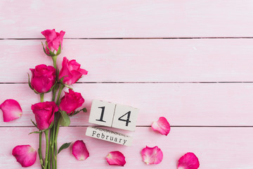 Valentines day and love concept. Pink roses with February 14 text on wooden block calendar on white wooden background.