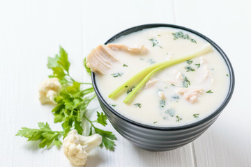 A bowl of cream of cauliflower soup with chicken broth on a white table.