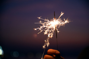 Happy cute girl holding a sparkler on beach during sunset. Celebration concept.