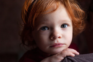 cute two year old girl with red hair sits on the hands of mom .close-up portrait