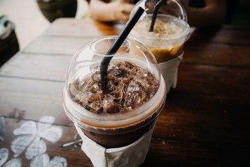 Close up of iced coffee and cocoa drink in plastic cup on wooden table.