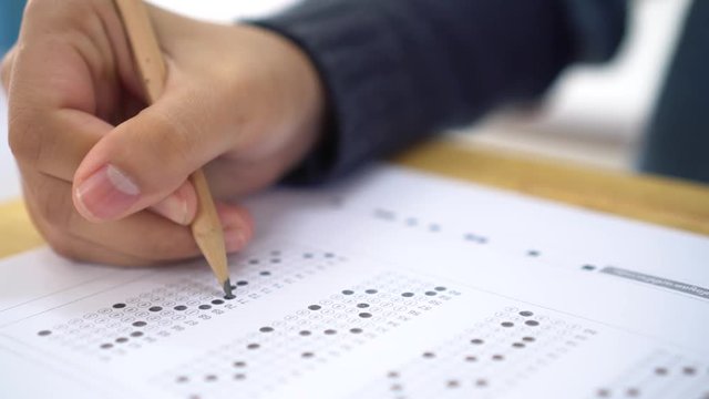School / university Students hands taking exams, writing examination room with holding pencil on optical form answers paper sheet on desk doing final test in classroom. Education assessment Concept