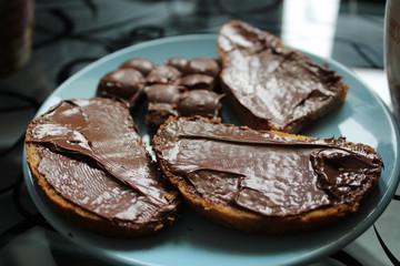 baguette with chocolate paste and pieces of chocolate on a blue plate