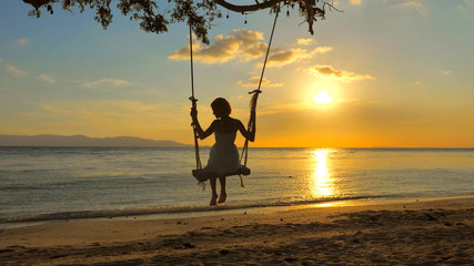 Back view Woman Silhouette on Swing,  Sea view with brightly Sunset colors on background