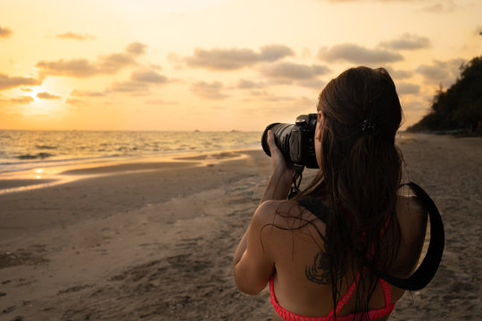 woman traveler on the shore of a tropical beach photographs the sunset on camera