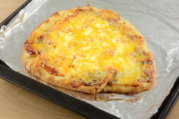 Naan bread pizza with melted cheese and sauce fresh out of oven on aluminum foil on baking sheet