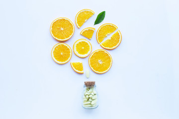 Vitamin C bottle and pills with orange fruit on white.