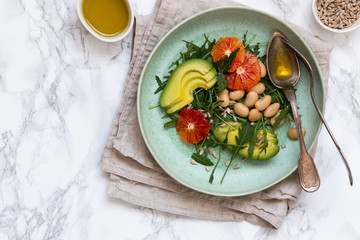 Vegan salad with rucola, seeds, avocado, orange and beans seasoned with olive oil. Healthy eating concept