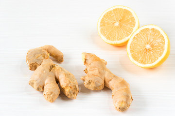 Closeup image of ingredients for natural cold or flu remedy includes ginger and lemon on a white wooden background. Selective focus on front slice of ginger 