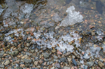 Pebble with ice on the beach. Small stones with ice on the river bank in spring.	