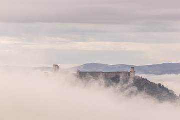 Naklejka na ściany i meble A view of Rocca Maggiore castle in Assisi (Umbria, Italy) in the middle of fog