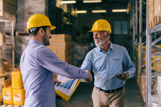 Two businessman with helmets on heads shaking hands for good finished job. Storage interior.
