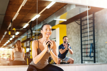 Close up of beautiful smiling Caucasian girl with ponytail doing exercises with kettlebell. In background mirror and man in reflection.
