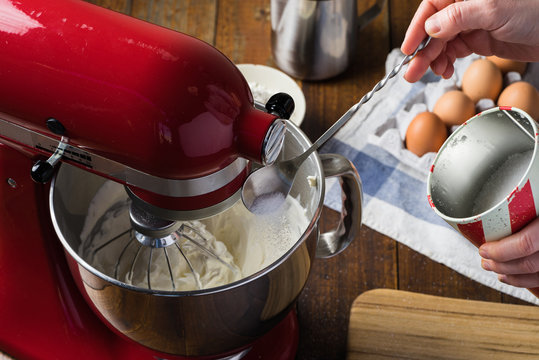 Pouring Sugar Into Bowl Of Red Standing Kitchen Aid Mixer On Wooden Table