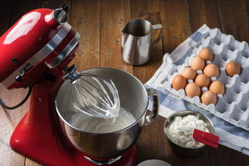 standing red mixer kitchen aid with cream on whisk. wooden table