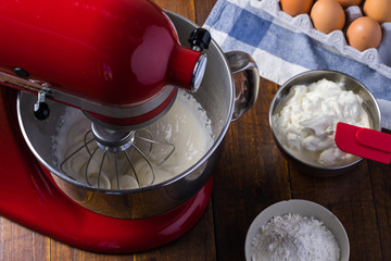 mixing red standing mixer kitchen aid on wooden table with cream cheese eggs glass flower