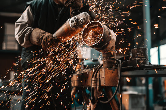 Unrecognizable man in protective suit and gloves cutting pipe with grinder. Workshop interior.