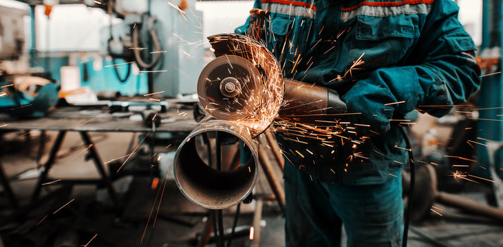 Close up of unrecognizable man in protective suit and gloves cutting pipe with grinder. Workshop interior.