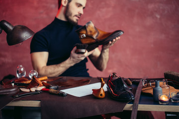 focus on polished leather shoe lying on the desk, handsome shoemaker on the blurred background, copy space