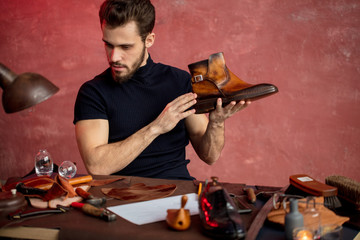 young shoemaker choosing the tool to repair boots, close up photo