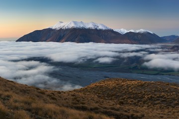 The valley is flooded in mist in a mountain environment. Over the fogs, only the high peaks of the mountains rise beneath the sunny sky. Misty morning on the Southern Island New Zealand, Christchurch 