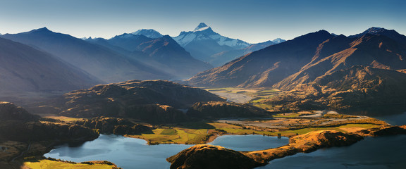 Obraz premium Panorama at sunset of Roys Peak between Wanaka and Queenstown with a lake and Mount Aspiring and cook of the new zealand alps on the background