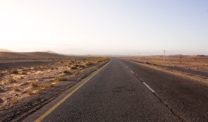 Highway through scenic desert of Jordan. High voltage powerlines along asphalt road in arid valley. Early morning in wilderness after sunrise. Electric power poles. Horizontal.