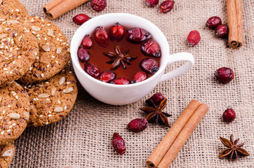 Oatmeal cookies with rosehip and aniseed tea. Cinnamon sticks, wild rose and anise against the background of burlap