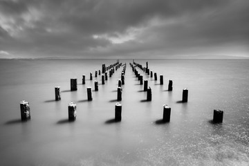 Wooden poles on Baltic Sea beach in high contrast evening light with clouds in windy weather, water movement in long exposure - Location: Baltic Sea, Rügen Island
