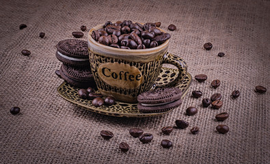 A cup of coffee with brown cookies on a background of burlap