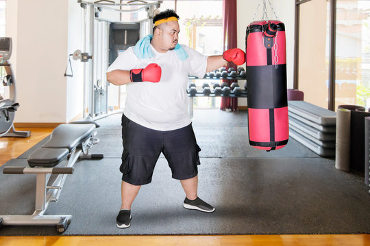 Obese Man Punches A Boxing Bag In Gym Center