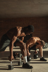 Fototapeta na wymiar Two multiracial male crossfit sportsmen with naked torso, exercising actively in sunny morning doing lunges with weights in both hands