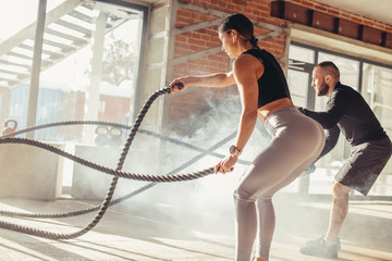 Caucasian fit attractive couple in sports clothing concentrated on the exercise with battle rope...