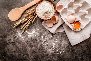 Baking ingredients with scattered flour on dark background with copyspace