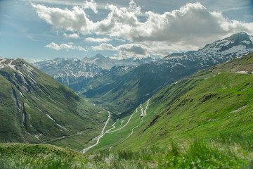 Obraz premium Sunny panoramic picture above Andermatt in Switzerland. A few streets towards the valley, green meadows and a few clouds.
