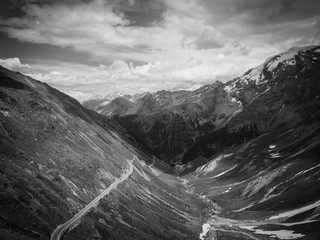 Stelvio Pass in Italy. Drone shot in the direction of the valley in summer. Green grass in a sunny atmosphere and a few clouds. Black and white.