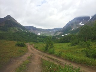 Old dirt road at the foot of mountains. The photo was taken in the caldera of the Vachkazhets volcano on the Kamchatka Peninsula, Russia.